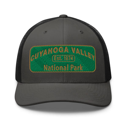 Cuyahoga National Park Hat with a green and gold embroidered national park styled patch on the front of a Yupoong 6606 charcoal/black trucker hat - front view.